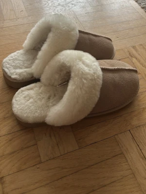 Beige fluffiga tofflor från H&M - Mysiga beige tofflor med päls på insidan och runt kanten, samt skinn utsidan. Storlek 37/38.