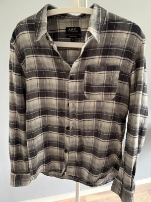 Overshirt APC - Snygg rutig skjorta från A.P.C. i svart, grått och vitt. Tillverkad i mjuk bomull med klassisk krage, bröstficka och knappar framtill. Perfekt för en avslappnad och stilren look. Storlek M i bra skick.