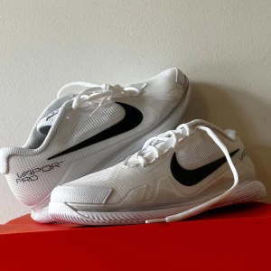 Tennisskor Nike - Säljer ett par Nike Zoom Vapor Pro HC i vitt och svart. Skorna har en stilren design med snörning och är perfekta för tennis eller paddel. De är helt nya och har en slitstark sula för bra grepp på banan.