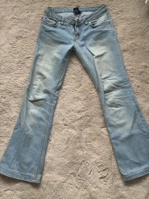 Ljusblå bootcut jeans från True Religion - Säljer ett par ljusblå bootcut jeans från True Religion med broderade detaljer på bakfickorna och klassisk femficksdesign. Jeansen har en normal passform och är tillverkade i bomull för en bekväm känsla. Perfekta för en avslappnad och trendig look.