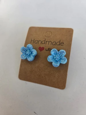 Handgjorda örhängen - glittriga ljusblå blommor  - Underbara små ljusblå blommor med massor av glitter! Perfekta till sommaren. Stiften är av rostfritt stål. Gjorda för hand av mig i polymerlera. 