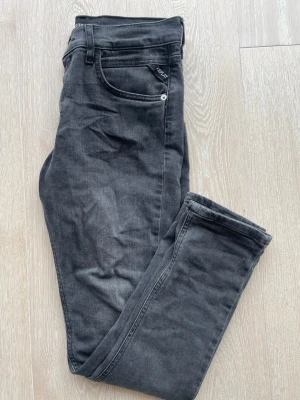 Svarta Replay jeans med smal passform - Snygga svarta jeans från Replay med klassisk femficksmodell och smal passform. Jeansen har en diskret tvättad look och är tillverkade i mjukt denimtyg med stretch för extra komfort. Perfekta för en trendig och avslappnad stil.