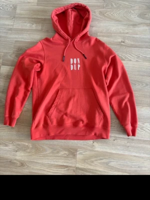 Orange hoodie från Dondup med tryck - Snygg röd hoodie från Dondup med vit logotyp på bröstet. Klassisk modell med huva och dragsnören samt en stor magficka framtill. Tillverkad i mjuk bomull som känns skön mot huden. Perfekt för en avslappnad och trendig stil.