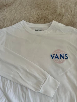 Vit långärmad topp från Vans - Vit långärmad topp från Vans med blå och rosa grafiskt tryck fram och stort tryck på ryggen. Storlek xs 