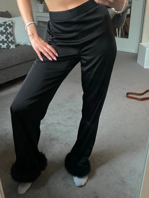 Svarta satinbyxor med päls - Svarta loungewear/pyjamas-byxor i satin med vida ben och fluffiga fuskpälsdetaljer längst ner. Super sköna. Pälsen går att ta av också🤗🤗