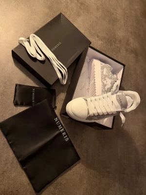 Vita sneakers från Numeris - Stilrena vita sneakers från Numeris med grått camomönster på sidan och bak. Skorna har tjock vit sula, vita skosnören och detaljer i både läder och textil. Märkeslogga på plösen och hälen. Perfekta för dig som gillar en clean men unik look. De är 44 men de passar för 43 ny pris på dessa 2700