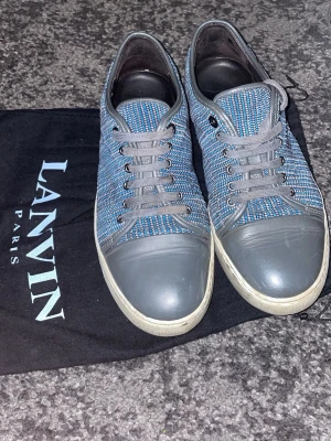 Blåa Lanvin sneakers box ingår ej storlek 41 - Snygga sneakers från Lanvin i blått och grått med textilovandel och grå gummitå. Skorna har grå snörning och vit sula. Perfekta för dig som vill ha en stilren och exklusiv look med en twist av streetstyle.