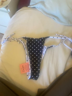 Svartvit prickig bikiniunderdel - Säljer en svart bikiniunderdel med vita prickar och knyt i sidorna. Klassisk tanga-modell med smala band och kontrasterande vit insida med svarta prickar. Helt ny oanvänd från shein.