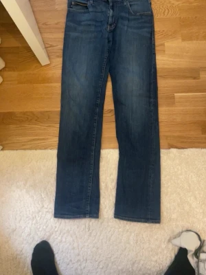 Blå raka jeans från Armani - Säljer ett par klassiska blå jeans från Armani med rak passform och fem fickor. Jeansen har en diskret logga på bakfickan och är tillverkade i denim med snygg tvätt. Perfekta för en avslappnad och stilren look.