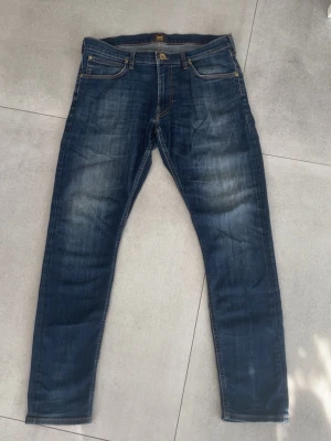 Lee jeans  - Tjo! Säljer ett par snygga blå  slim fit jeans från Lee med klassisk femficksdesign och slitna detaljer framtill. Jeansen har kontrastsömmar och metallknappar. Tillverkade i denim med en tvättad look som ger en as go outfit. Modellen är luke som är en av de bättre modellerna till och med🤗skicket är som helt nytt 10/10 och storleken är w34 L32! Hör av dig vid mer frågor eller funderingar🤩mvh Ga