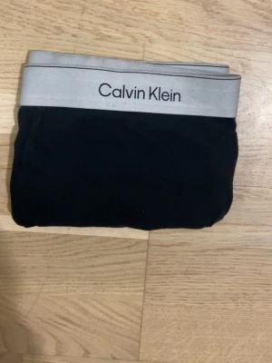 Svarta kalsonger från Calvin Klein - Snygga svarta kalsonger från Calvin Klein med bred grå resår och logga framtill. Tillverkade i mjuk bomull med lite elastan för extra komfort och bra passform. Perfekta för dig som gillar stilrena och klassiska underkläder.