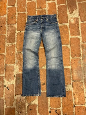 Blå raka/bootcut  jeans från Levi's - Ett par blå vintage-jeans i bootcut-modell från Levi’s som passar både män och kvinnor. Jag är osäker på vilken modell det är eftersom jeansen saknar etiketten på baksidan. Förutom att etiketten saknas känns jeansen tjocka och robusta och visar knappt några tecken på slitage!   Midja: 37 cm Innersöm: 25 cm Total längd: 101 cm Lårbredd: 22 cm