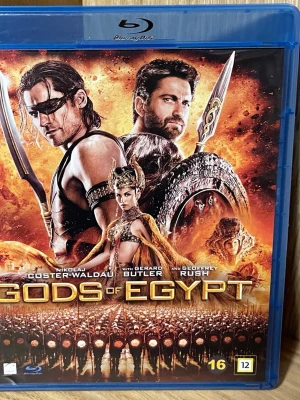 Gods of Egypt Blu-ray film - Blu-ray film med titeln 'Gods of Egypt'. Omslaget har en actionfylld illustration med gudar, svärd och sköldar i eldiga färger. Filmen är klassad som actionäventyr och har åldersgräns 16 år. Text på svenska, engelska och finska finns på baksidan.