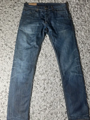 Blå skinny dondup jeans med slitningar - Säljer ett par blå jeans med raka ben och snygga slitningar. Jeansen har klassisk femficksmodell och normal midja. Materialet är denim i bomull och färgen är tvättad blå med ljusare partier. Perfekta för en avslappnad och trendig stil. Längd: 107 cm midja: 41 cm