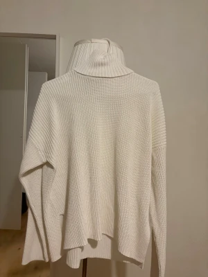 Vit polotröja i grovstickat - Säljer en oversized vit stickad polotröja med breda ärmar och hög krage. Tröjan har en grovstickad struktur och är riktigt mjuk och skön. Perfekt för kalla dagar när du vill vara både varm och stilren.