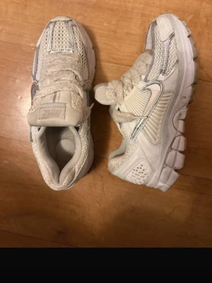 Nike vita mesh sneakers - Nike sneakers i vitt med meshpaneler och detaljer i silver. Skorna har en chunky sula och klassisk snörning. Swoosh-logga på sidan och ventilerande material för extra komfort. Perfekta för dig som gillar sportig och trendig stil.