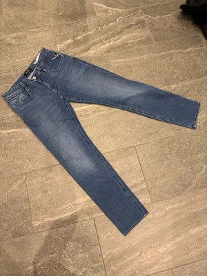 Sprillans nya Replay anbass - Snygga blå jeans från Replay med klassisk femficksdesign och dragkedjegylf. Jeansen har en smal passform och är tillverkade i stretchigt denimtyg för extra komfort. Perfekta för en trendig och avslappnad look.