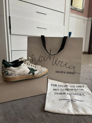 Golden Goose vita sneakers med grön stjärna - As snygga Golden Goose sneakers i vitt läder med grön stjärna på sidan, gröna detaljer vid hälen och beige sula. Skorna har silverfärgade partier vid tån och hälen samt klassiska snörningar. Snygg retrostil och coola detaljer.