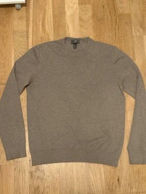 Beige stickad tröja från H&M - En stilren beige stickad tröja från H&M med rund halsringning och långa ärmar. Tröjan har en enkel och klassisk design med ribbade muddar vid ärmslut och nederkant. Perfekt basplagg i mjukt material.