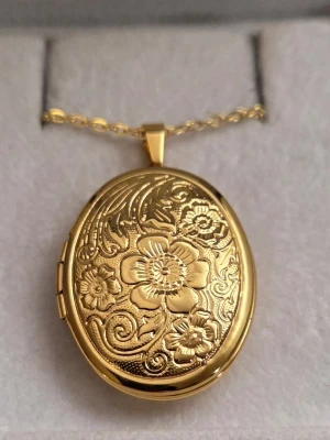 Guldfärgat medaljonghalsband med blommor - Lite limrester i kanterna (se bilder) inget som påverkar skick eller funktion men har sänkt priset pga detta. 🌸// Snyggt guldfärgat medaljonghalsband med oval form och detaljerat blommönster på framsidan. Medaljongen går att öppna och har plats för ett litet foto eller minne. Kedjan är tunn i rostfritt stål och matchar medaljongens eleganta stil. Perfekt accessoar för dig som gillar vintagevibbar och unika smycken.
