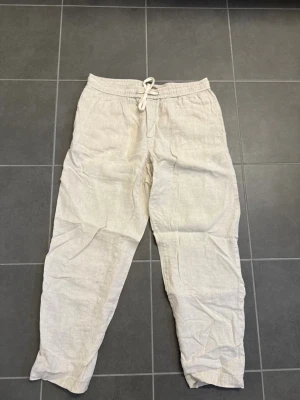 Beiga linnebyxor från Mango, stl S - Säljer ett par beiga linnebyxor med avslappnad passform och elastisk midja med dragsko. Byxorna har raka ben och sidofickor. Perfekta för en chill och stilren look under varma dagar.