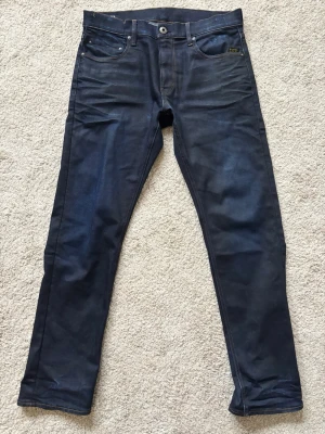 G-Star Jeans - Säljer ett par mörkblå G-Star jeans, modell Mosa Straight Jeans. Storlek W33/L32. Använd endast ett fåtal gånger. Regular straight fit, tillverkade i slitstarkt denim. Hör av dig vid funderingar 🤩