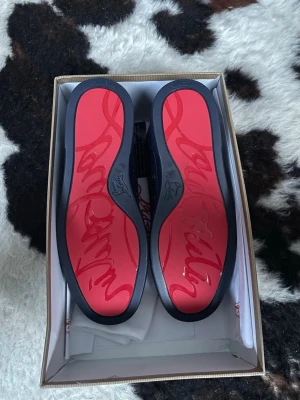 Marinblåa sneakers från Christian Louboutin - Snygga marinblåa sneakers från Christian Louboutin med klassisk röd sula och diskret logga. Skorna har en låg profil, är tillverkade i mocka och har blåa snören. Perfekta för dig som vill ha en exklusiv och stilren look.