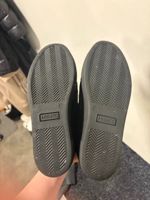 Svarta sneakers från Axel Arigato - Snygga svarta sneakers från Axel Arigato i mocka med kardborreband över vristen. Skorna har en låg silhuett och robust gummisula med tydligt mönster. Perfekta för dig som gillar minimalistisk och stilren design.