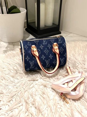 Denim monogram handväska - Säljer en snygg blå handväska i denim-look med klassiskt monogrammönster. Väskan har ljusa läderhandtag och detaljer samt avtagbar axelrem. Perfekt cylinderformad modell som rymmer det viktigaste och ger en trendig touch till din outfit. Endast 3 i lager alltså 3 lyckliga tjejer kommer att äga denna. Priset är endast för en :) 