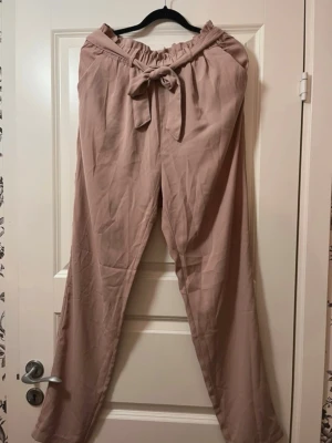 Gammelrosa/ljusrosa byxor med knyt från BikBok - • Använd vid ett tillfälle, nypris 299kr• Säljer ett par gammelrosa/ljusrosa byxor från BikBok i storlek M. Byxorna har hög midja med resår och ett brett knytband framtill. De är vida i modellen och har en mjuk, luftig känsla som passar perfekt till sommaren. Materialet är tunt och skönt.