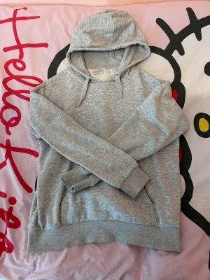 Ljusgrå hoodie med huva - En stilren ljusgrå hoodie från Gina Tricot med klassisk huva och dragsnören. Hoodien har ribbade muddar vid ärmslut och nederkant samt en stor magficka framtill. Tillverkad i mjukt bomullsmaterial som är skönt mot huden. Perfekt för en avslappnad och casual look. Köpte för ungefär 300kr.
