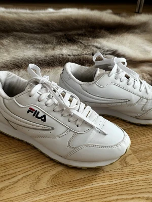 Sneakers från FILA - Säljer ett par klassiska vita sneakers från FILA. Perfekta för dig som gillar en clean och sportig look. 37