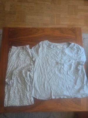 Ljusgrå pyjamas med prickigt mönster - Mysig pyjamas i ljusgrått med kortärmad tröja och byxor. Tröjan är enfärgad och har rund halsringning, medan byxorna har ett diskret prickigt mönster i vitt och grått. Perfekt för chillkvällar hemma.