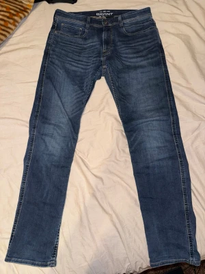 Blå jeans från Grant W32 L32 - Snygga blå jeans från Grant i klassisk rak modell. Jeansen har fem fickor, gul kontrastsöm och en tvättad look med lätt slitning. Tillverkade i denim som ger en skön passform och stilren vibe.
