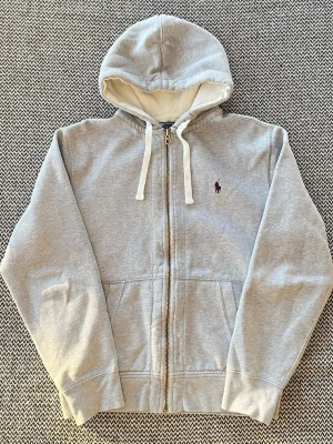 Grå Ralph Lauren hoodie med dragkedja i storlek M - Grå Ralph Lauren hoodie med dragkedja och vinröd logga helt utan defekter  Hör av er vid frågor!