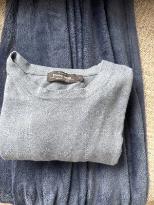 Ljusblå stickad tröja Dressmann - Ljusblå stickad tröja från Dressmann med rund halsringning och långa ärmar. Tröjan har en enkel, stilren design och ribbade muddar vid ärmslut och nederkant. Perfekt för lager på lager och passar till både jeans och chinos.