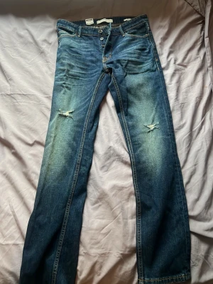 Blå slitna slim jeans från MNG MAN - Ett par blå slim fit jeans från MNG MAN med slitningar på båda knäna och snygga tvättade detaljer. Klassisk femficksmodell med knappgylf och raka ben. Tillverkade i bomull med en cool, avslappnad vibe. Jeansen är helt nya med lappar kvar.