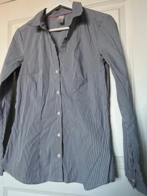 Svart/vit randig H&M skjorta - Bekväm, figurnära och fin svart/vit randig skjorta från H&M. I väldigt bra skick. Storlek 40, normal i storleken. Passar även 36/38, men en lösare passform. Original extra knapparna kommer med (bild 3).