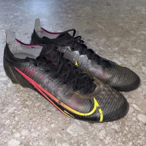 Nike Mercurial fotbollsskor Elite Acc FG - Säljer ett par Nike Mercurial fotbollsskor i svart med gula och röda detaljer. Skorna har låg profil, snörning och en tunn syntetisk ovandel för bra bollkontroll. Snygg design med Nike-logga på sidan och tå. Perfekta för dig som vill ha speed på planen. Skick: 8/10 (Lite smutsiga)