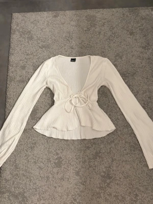 Vit omlottopp med knyt och v-ringning - Supersnygg vit omlottopp med djup v-ringning och långa ärmar som svänger ut nertill! Väldigt fin och inga direkta synliga effekter🫶🏼