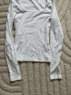 Vit ribbad långärmad topp - Säljer en vit ribbad topp med lång ärm och fyrkantig ringning. Toppen har en slim passform och är tillverkad i mjuk bomull, perfekt att styla med jeans eller kjol. Enkel och stilren design som passar till många olika looks.