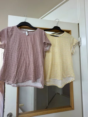 Två randiga t-shirts i bomull - Säljer två snygga t-shirts i mjuk bomull. Ena är vit med tunna röda ränder och den andra är vit med tunna gula ränder. Båda har rund halsringning, korta ärmar och en avslappnad passform. Perfekta till jeans eller shorts för en chill look.