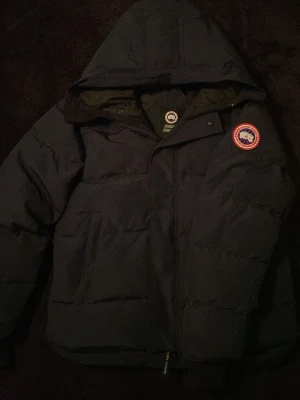 Mörkblå dunjacka från Canada Goose - Tjena! 👋  Säljer en helt ny Canada Goose-jacka då den tyvärr inte passade mig som jag hade tänkt. Jackan är i nyskick och har aldrig använts – endast provad. Alla detaljer är i toppskick och den är precis som när den köptes.  Perfekt inför kalla dagar då Canada Goose är kända för sin höga kvalitet, värme och stilrena design.  Hör gärna av dig vid intresse eller om du vill ha fler bilder! 😊