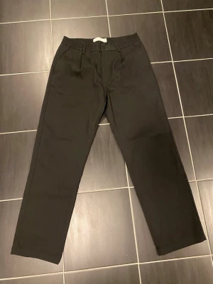 Svarta kostymbyxor Bershka - Snygga svarta kostymbyxor med rak passform och resår i midjan för extra komfort. Byxorna har diskreta sidfickor fram och två fickor bak. Perfekta för en clean och stilren look. Materialet ser ut att vara en mjuk och följsam bomullsblandning. Mycket fint skick, storlek M!