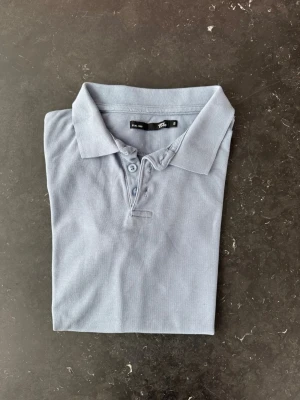 Ljusblå pikétröja från Lager157 - Klassisk ljusblå pikétröja från lager157 med krage och knappar framtill. Tillverkad i mjuk bomull och har korta ärmar. Perfekt för en avslappnad men ändå stilren look.