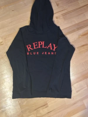  hoodie från Replay -  Snygg hoodie från Replay med stor röd logga och texten 'BLUE JEANS' på bröstet. Klassisk huva och lång ärm, perfekt för en avslappnad streetwear-look. Tillverkad i mjukt material som känns skönt mot huden.