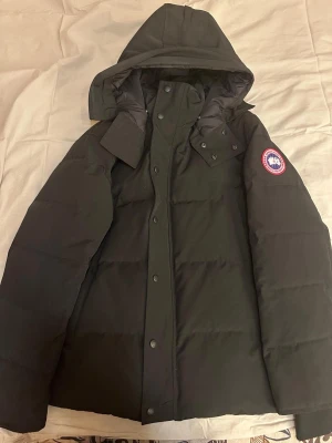 Svart parkas från Canada Goose - Snygg svart parkas från Canada Goose med avtagbar huva och pälsdetalj. Har råkat beställa fel storlek och jackan har endast suttit på hyllan helt oanvänd och ännu helt ny. Pris kan diskuteras skriv bara vid intresse