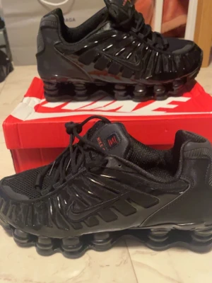 Nike Shox svarta sneakers - Säljer ett par  helt nya oandvända svarta Nike Shox sneakers med cool fjädrande sula och detaljer i blankt och matt material. Skorna har mesh- och syntetpaneler, snörning och diskret Nike-logga på sidan. Perfekta för dig som gillar sportig och futuristisk stil. Storlek 43. Ej RIKTIGA