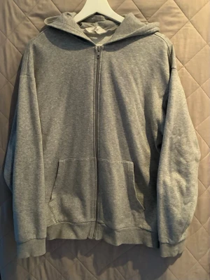 Grå zip zip hoodie - En grå zip hoodie med dragkedja från HM.  Hoodien är väldigt skön och stilig. Tillverkad i mjukt bomull. Strl M.