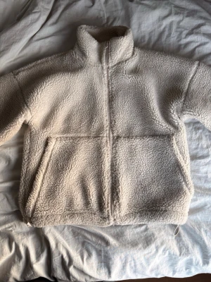 Beige teddyjacka med dragkedja - Mysig beige teddyjacka i fluffigt material med hög krage och hel dragkedja framtill. Jackan har två stora fickor på sidorna och en avslappnad passform. Perfekt för kalla dagar när du vill vara både varm och stilren. Köptes för 800, då skicket inte är nyskick säljer jag för 300🥰
